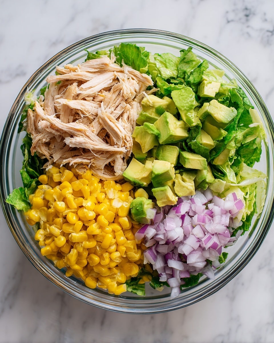 A clear glass bowl on a white marbled surface shows a fresh salad with five main sections. At the bottom left, there is bright yellow corn with a shiny texture. Above the corn, shredded light tan chicken lies in a slightly messy pile. To the right of the chicken, green avocado pieces cut into small cubes are scattered. Next to the avocado, fresh green lettuce leaves add a crisp and leafy layer. In the center, finely chopped light purple onions form a small pile over the other layers. The bowl displays these colorful, fresh ingredients clearly from above. photo taken with an iphone --ar 4:5 --v 7