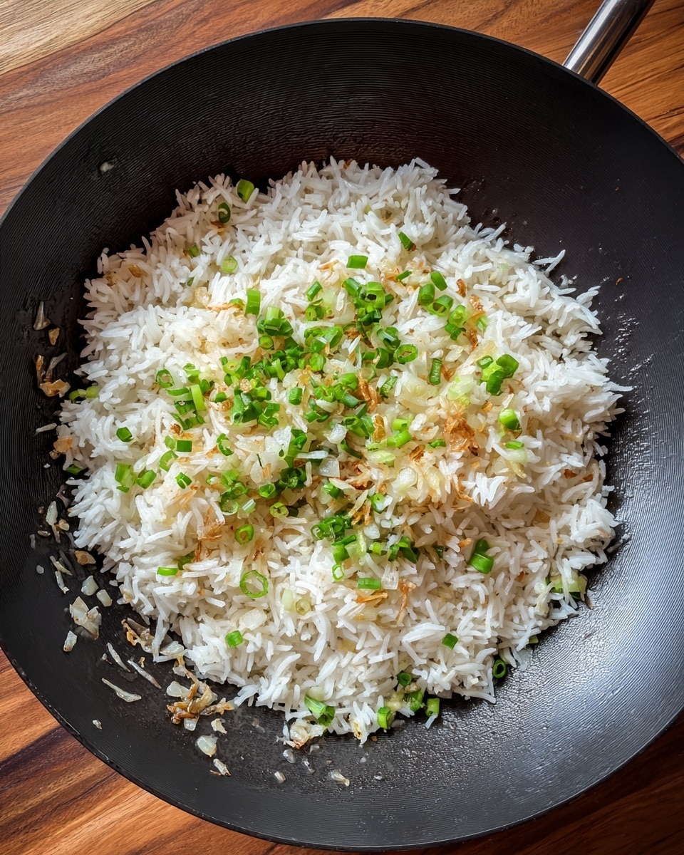 A black wok holds a layer of white cooked rice sitting on top of small pieces of light brown and pale green cooked onions, with some oily sheen on the surface of the wok. The rice appears fluffy with distinct grains, and the onions are spread evenly beneath it. The wok is set on a wooden surface. photo taken with an iphone --ar 4:5 --v 7