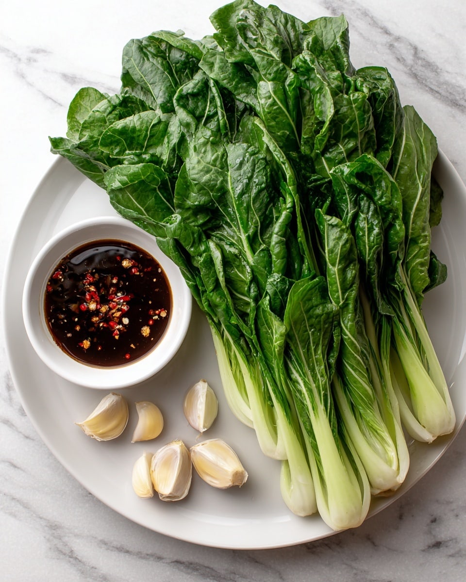 A white plate filled with a bunch of fresh yu choy, arranged so that the green leafy tops fan out and the thick pale stems are gathered closely together at the bottom right side of the plate, placed on a white marbled surface. To the left of the plate is a small white bowl containing dark brown garlic sauce with visible red chili flakes floating on top. Below the bowl, three whole garlic cloves are spread out on the white marbled surface. Text labels appear next to each main element. Photo taken with an iphone --ar 4:5 --v 7