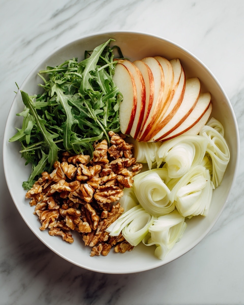 A white bowl filled with four layers arranged side by side: thinly sliced light green fennel with smooth, curled edges at the bottom right, a pile of brown toasted walnuts with an uneven texture next to it on the left, fresh dark green arugula leaves with a slightly jagged shape on the far left, and a stack of thinly sliced apple pieces with a pale cream inside and bright red edges on the top right. The bowl is set on a white marbled surface. photo taken with an iphone --ar 4:5 --v 7