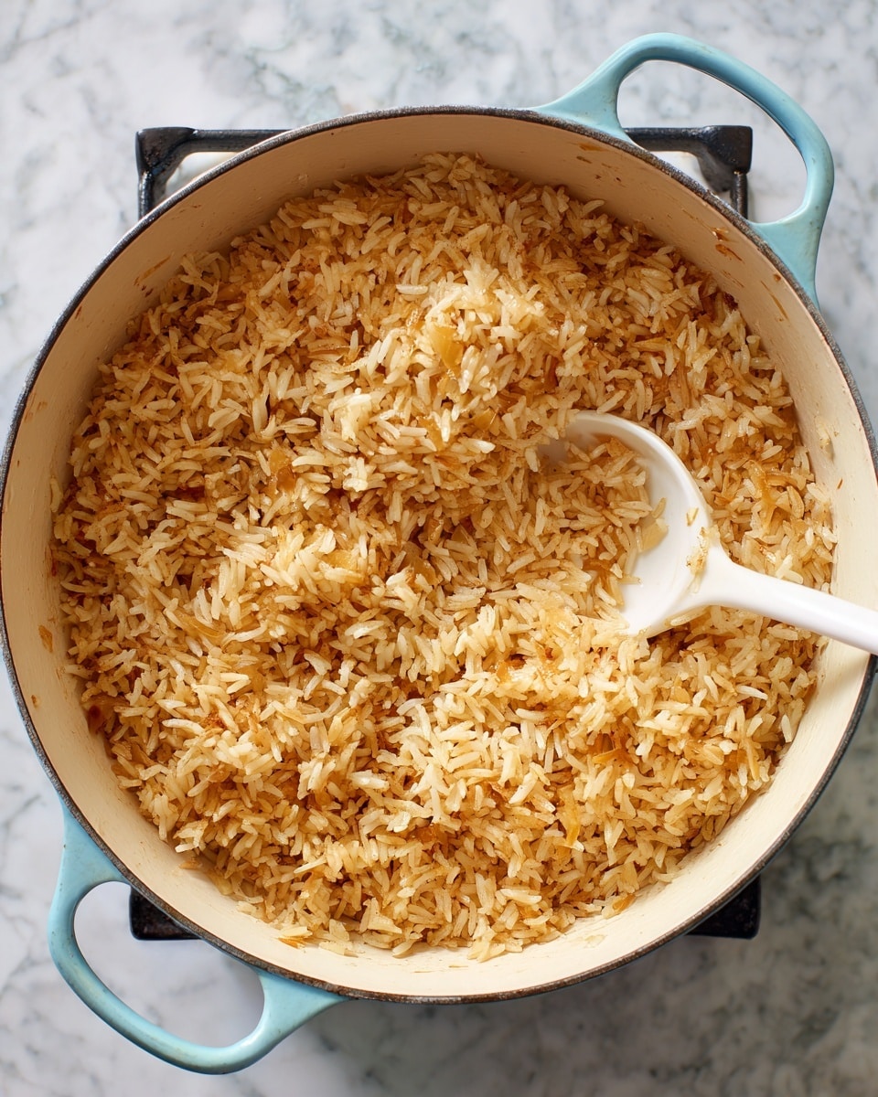A white pot filled with a single layer of golden brown toasted rice mixed with small bits of chopped onion scattered evenly throughout. A white spoon is partially resting inside the pot on the right side, stirring the rice and onions. The pot handles are light blue, and the pot sits on a stove with a black surface. The background is a white marbled texture. photo taken with an iphone --ar 4:5 --v 7