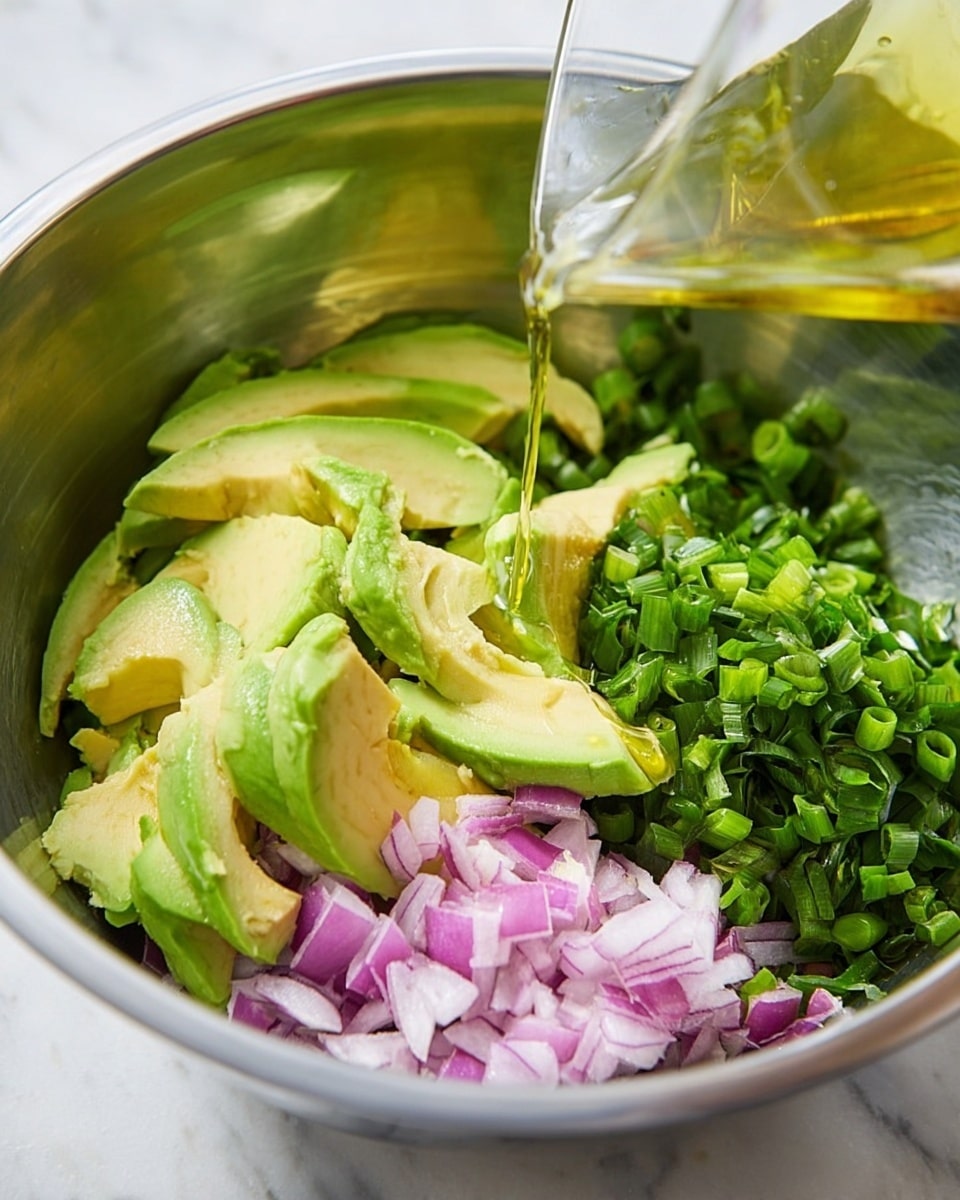A metal bowl contains several layers of fresh ingredients: the first layer has large, peeled avocado slices with a soft green and yellow texture, placed in the center and front; next to the avocado, finely chopped red onion slices with a smooth, purple texture are spread on the right side; behind them, a layer of bright green chopped spring onions covers the upper right area. A clear glass container is pouring light golden oil or dressing onto the avocado, creating a small pool in the middle. The bowl sits on a white marbled surface. photo taken with an iphone --ar 4:5 --v 7