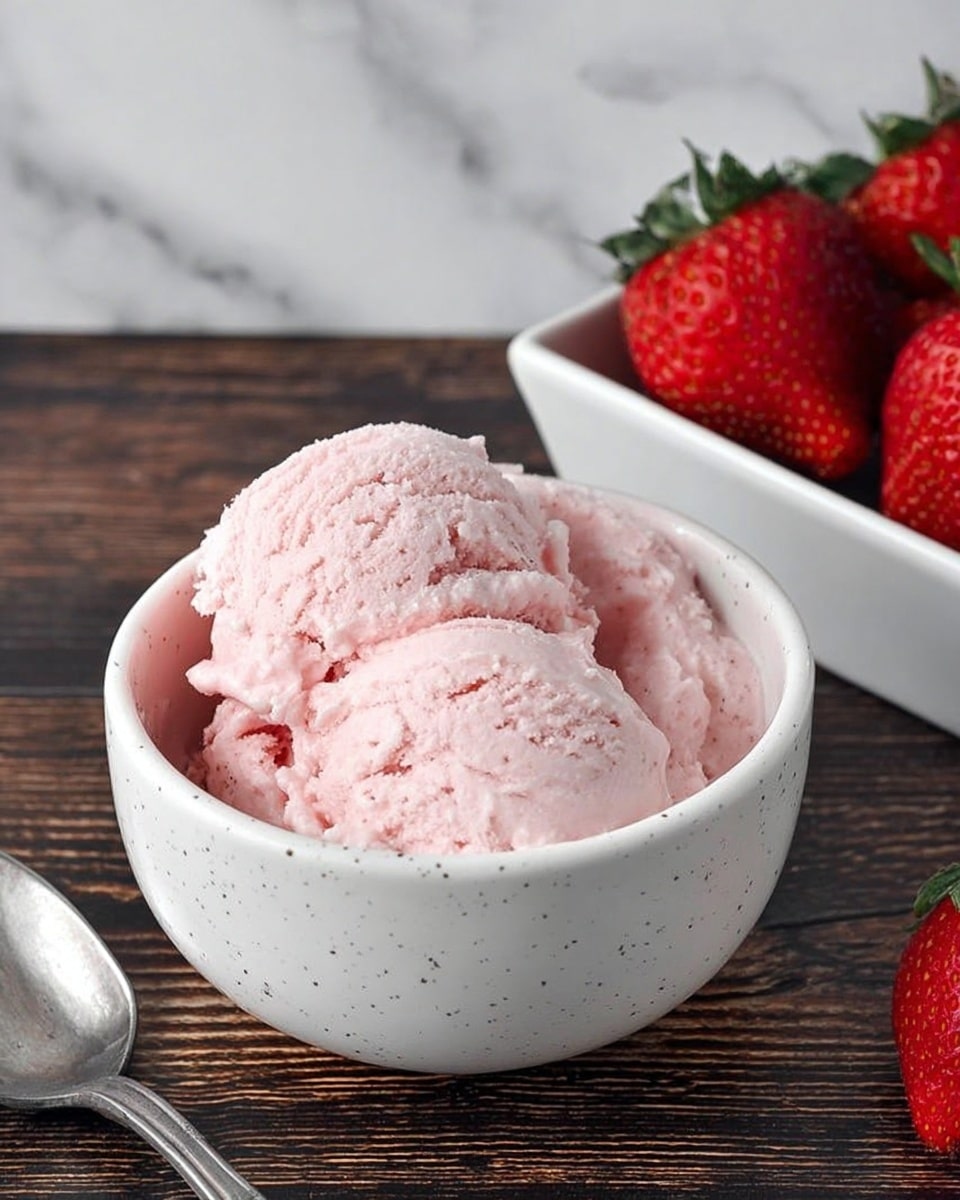 The image shows a white speckled bowl filled with two scoops of light pink creamy ice cream, with a smooth and slightly fluffy texture, placed on a dark wooden surface. Next to the bowl, there is a white rectangular dish holding fresh red strawberries with green tops, and a metal spoon resting beside the bowl. The background is a white marbled texture. photo taken with an iphone --ar 4:5 --v 7