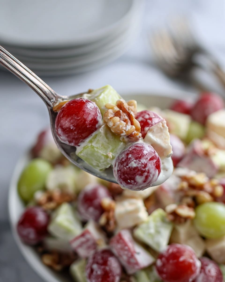 A close-up of a spoon holding a mixture of salad with visible layers of red and green grapes, light beige cheese cubes, and brown walnuts, all coated in creamy white dressing. The spoon is held above a white bowl filled with the same salad mix, showing the round, juicy grapes and the creamy coating that clings to the pieces. In the blurry background, there are stacked white plates and a white marbled surface. The overall look is fresh and colorful with soft lighting. photo taken with an iphone --ar 4:5 --v 7
