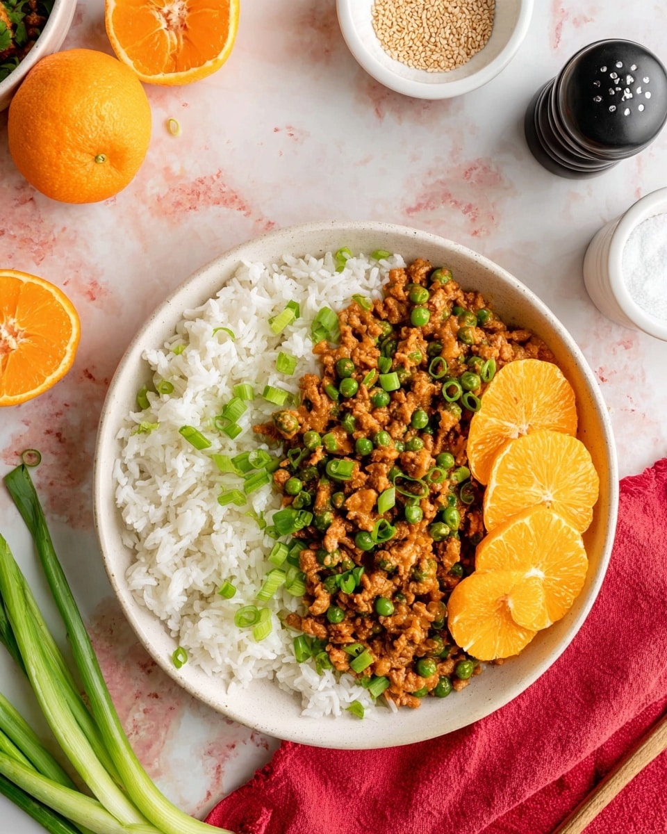 A white bowl is filled with a base layer of fluffy white rice. On top of the rice, there is a layer of cooked ground meat mixed with green peas, all covered in a brown sauce. Bright green chopped spring onions are sprinkled evenly over the meat mix, adding a fresh contrast. Two thin, bright orange slices rest on the right side of the bowl. The bowl sits on a white marbled surface, surrounded by a red cloth, two orange halves, a small white bowl of sesame seeds, black and white salt and pepper shakers, and some whole green spring onions. Photo taken with an iphone --ar 4:5 --v 7