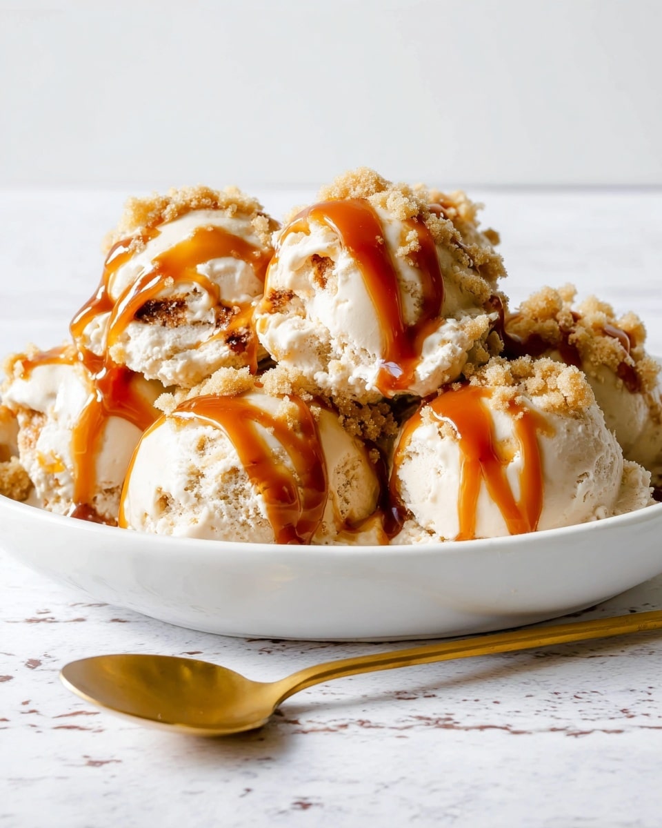 The image shows several scoops of light beige ice cream with a crumbly texture layered inside each scoop. On top, thick, shiny caramel sauce is drizzled unevenly, creating rich golden brown streaks flowing over the ice cream and crumbs. The scoops are served close together in a smooth white dish placed on a white marbled surface. In the front, a shiny golden spoon is resting on the same white marbled texture, adding a touch of elegance. The background is simple and clean with a white marbled look. Photo taken with an iphone --ar 4:5 --v 7
