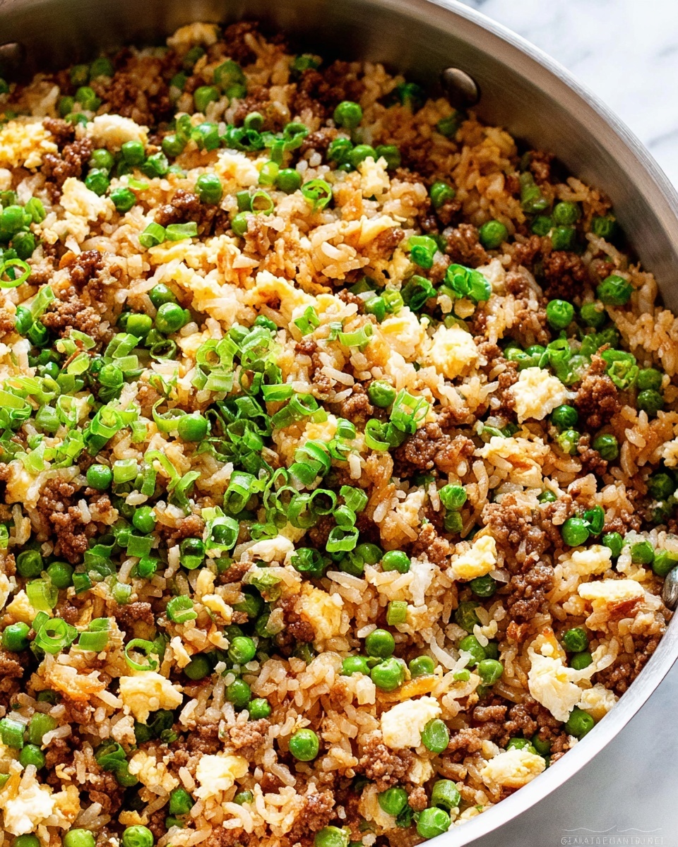 The image shows a close-up of fried rice in a large silver pan. The dish has several layers: lightly browned rice, cooked ground meat mixed evenly throughout, bright green peas scattered around, chopped green onions on top, and small pieces of scrambled egg mixed in. The textures look soft with some crunchy green onion bits. The background surface is a white marbled texture. photo taken with an iphone --ar 4:5 --v 7