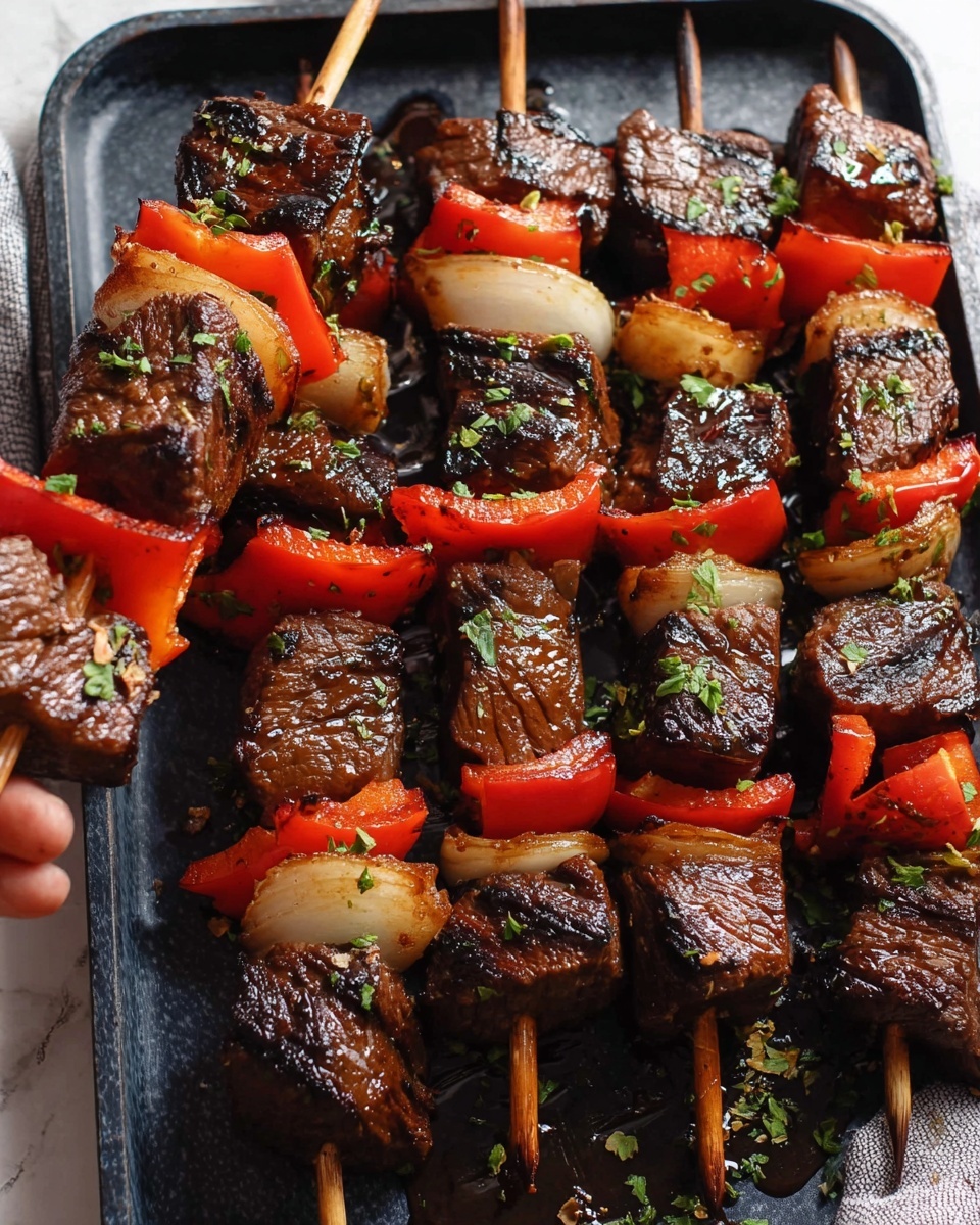 Several skewers with three layers on each, placed on a dark grill pan over a white marbled surface. Each skewer has large grilled dark brown meat cubes with a shiny glaze, alternating with bright red bell pepper pieces and light brown onion slices that have slight char marks. Some green herb sprinkles are scattered over the meat and vegetables. A woman's hand holding one skewer with a piece of red bell pepper close to the camera is visible on the left side. The texture of the meat looks slightly rough and cooked, the vegetables look soft with some areas caramelized from grilling. photo taken with an iphone --ar 4:5 --v 7