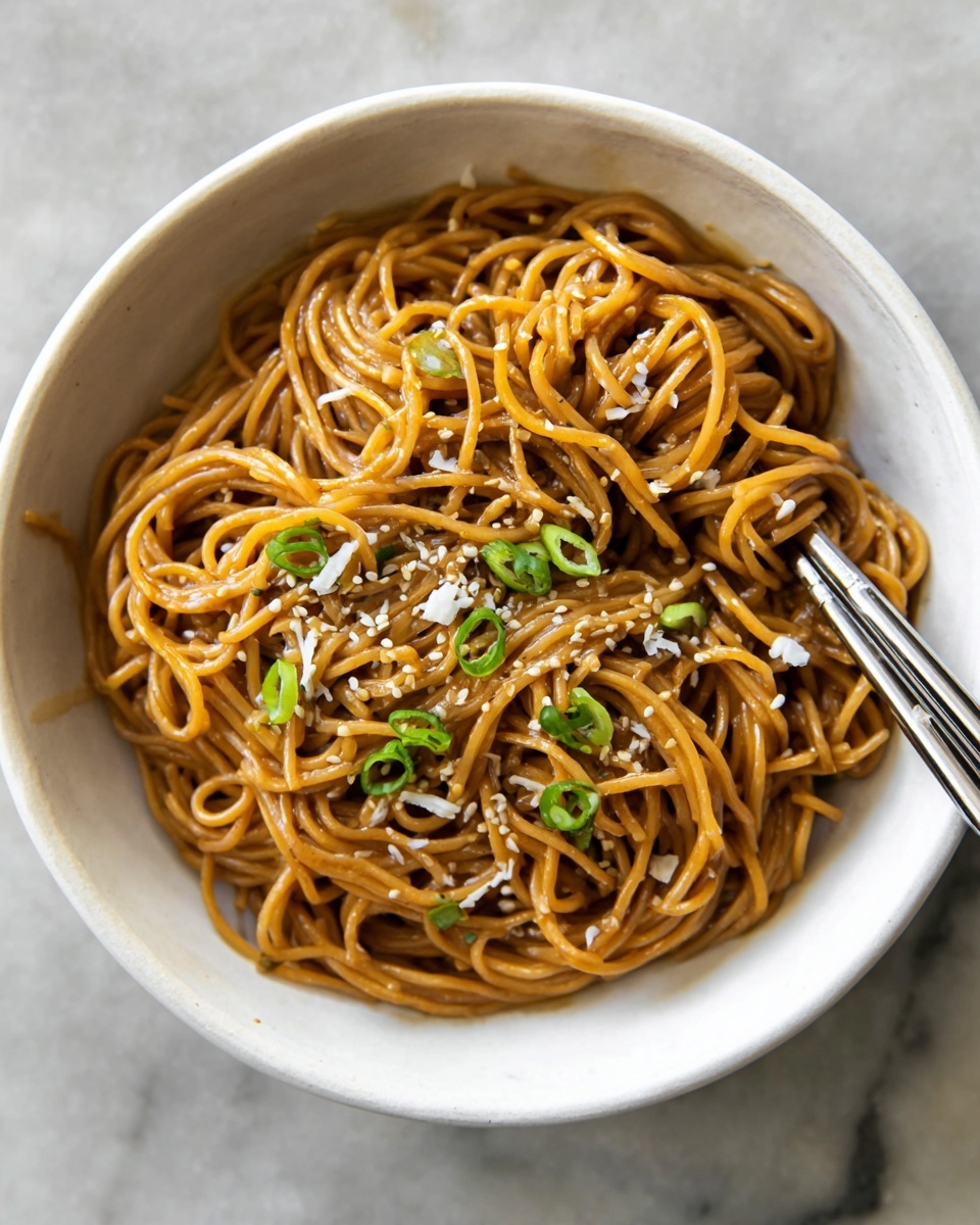 A bowl of glossy brown noodles layered in a messy pile fills the white bowl. The noodles are thin and coated in sauce, topped with a light sprinkle of finely shaved white cheese and small pieces of green herbs scattered around. The bowl rests against a soft white marbled surface with a blurred cloth in the background. A pair of silver chopsticks poke out from the right side of the bowl. photo taken with an iphone --ar 4:5 --v 7