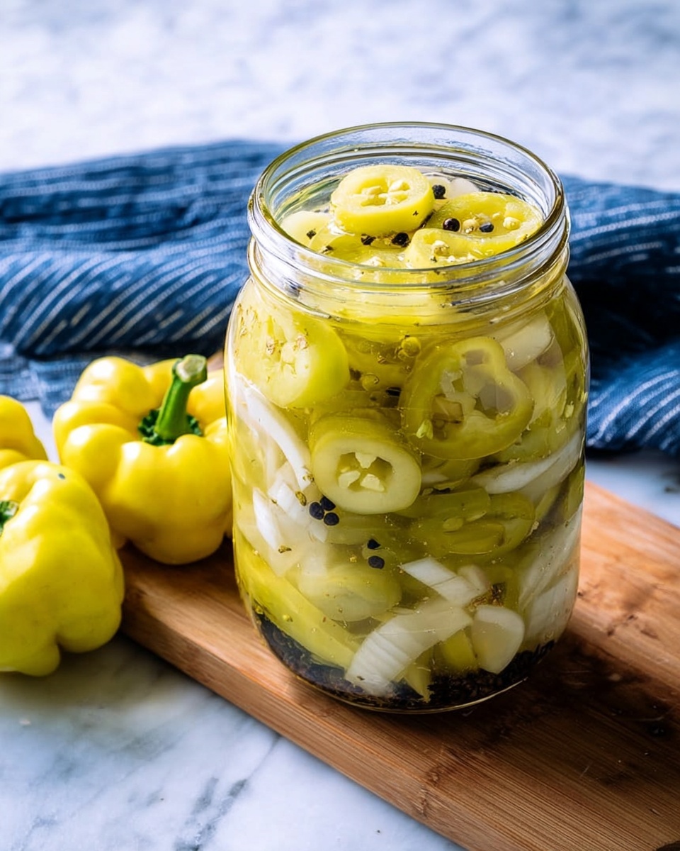 A clear glass jar filled with layers of round yellow-green pepper slices, white onion pieces, and scattered small black peppercorns, all submerged in a light yellowish-green pickling liquid. The jar sits on a white marbled surface with a wooden board in the background holding three whole yellow peppers on a blue and white striped cloth. photo taken with an iphone --ar 4:5 --v 7