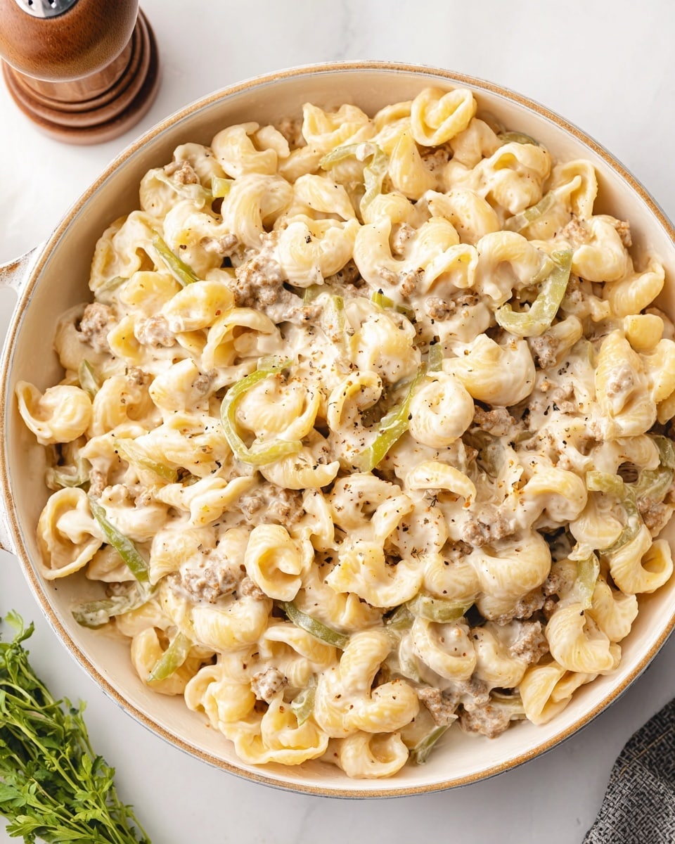 A white round pan filled with creamy pasta shows three main layers: the pasta, which is curved and pale yellow, forms the bulk of the dish; small pieces of cooked ground meat, light brown in color, are spread evenly throughout; and thin green bell pepper slices add subtle color contrast, all coated in a creamy white sauce, giving it a smooth texture. The pan sits on a white marbled surface with a small bunch of green herbs and a wooden pepper grinder nearby. Photo taken with an iphone --ar 4:5 --v 7