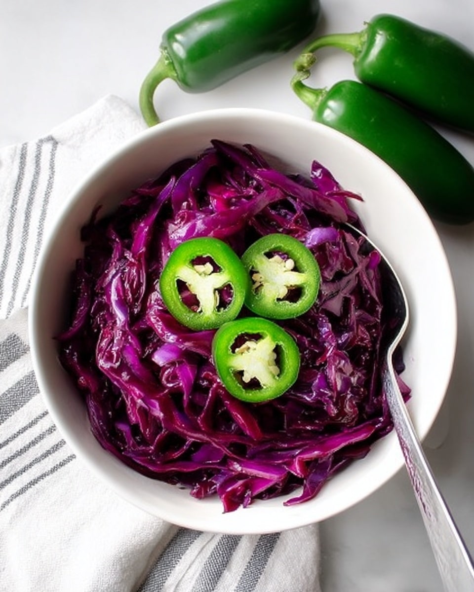 A white bowl filled with thin strips of deep purple cabbage layered tightly with a glossy texture, topped with three bright green jalapeño slices showing seeds in the center, a silver spoon rests inside the bowl on the right side, the bowl sits on a white cloth with thin gray stripes on a white marbled surface, three whole green jalapeños are placed beside the bowl, photo taken with an iphone --ar 4:5 --v 7