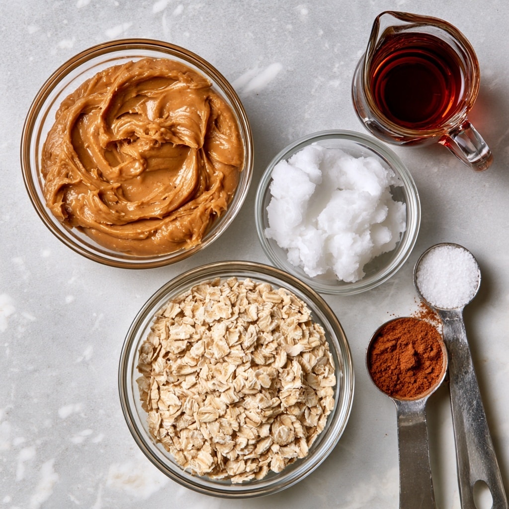 The image shows six clear glass bowls and one metal measuring spoon arranged neatly on a light grey surface with a white marbled texture. The largest bowl at the bottom center contains light beige old fashioned rolled oats with a rough texture. Above it and to the left is a medium bowl filled with smooth light brown peanut butter showing swirled patterns. At the top right is a small glass pitcher holding dark amber maple syrup with a shiny surface. Just below the syrup is a small bowl filled with solid white coconut oil that appears soft and fluffy. To the right of the oil, there is a silver measuring spoon with white salt, and beneath it a slightly larger silver measuring spoon filled with finely ground reddish-brown cinnamon. Each ingredient is isolated in its container with clear visibility of texture and color, all placed on a simple white marbled background. Photo taken with an iphone --ar 4:5 --v 7
