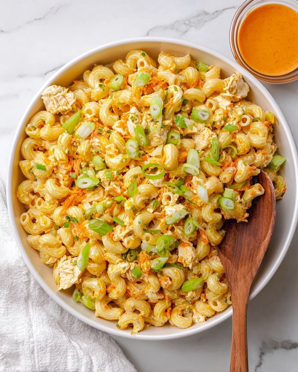 A large white bowl filled with three layers of creamy macaroni salad. The base layer is pale yellow elbow macaroni mixed with small green celery pieces and orange shredded carrot bits. The middle layer shows chunks of light beige chicken mixed evenly with the pasta. The top layer is garnished with thin slices of bright green onions scattered over the dish. A wooden spoon rests on the right side inside the bowl, partly submerged in the salad. To the top right beside the bowl, there is a small clear glass bowl with orange dressing on a white marbled surface, next to a white cloth. Photo taken with an iphone --ar 4:5 --v 7