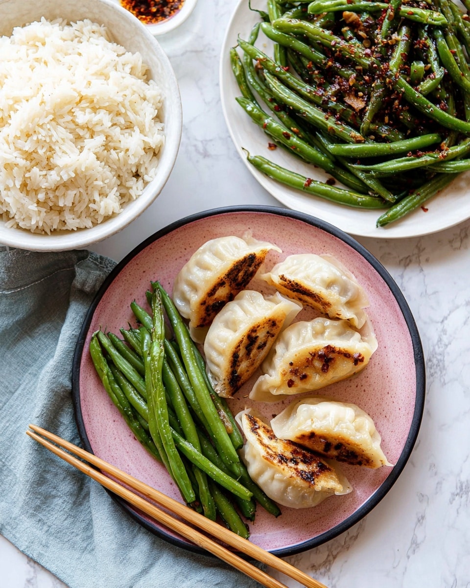 The image shows a meal with three main dishes arranged on a white marbled surface. On the left, there is a white bowl filled with fluffy white rice, placed on a light blue napkin. To the right, a white plate holds vibrant green sautéed green beans sprinkled with minced garlic and red pepper flakes. In the foreground, a pink plate with a dark rim features six pan-fried dumplings, each with golden brown crispy spots and a light sauce drizzled on top, sitting next to a small bunch of the sautéed green beans. A pair of wooden chopsticks rests between the bowls and plates, crossing the surface. photo taken with an iphone --ar 4:5 --v 7