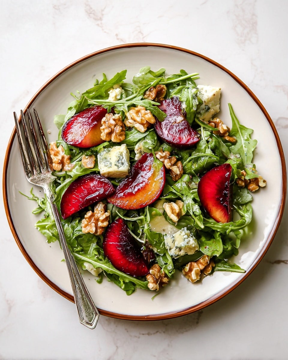 A vibrant salad is shown on a white plate with a brown rim, placed on a white marbled surface. The salad has three main layers: the bottom layer is bright green arugula leaves with a fresh, slightly curly texture; the middle layer has deep red and purple plum slices, cut in half showing smooth shiny skin and juicy flesh; the top layer includes light brown walnut pieces scattered throughout and small white creamy chunks of cheese with blue veining. A shiny silver fork rests on the left side of the plate. The colors of green, red, and light brown mix with the white plate and marbled background, giving a fresh and vibrant look. Photo taken with an iphone --ar 4:5 --v 7
