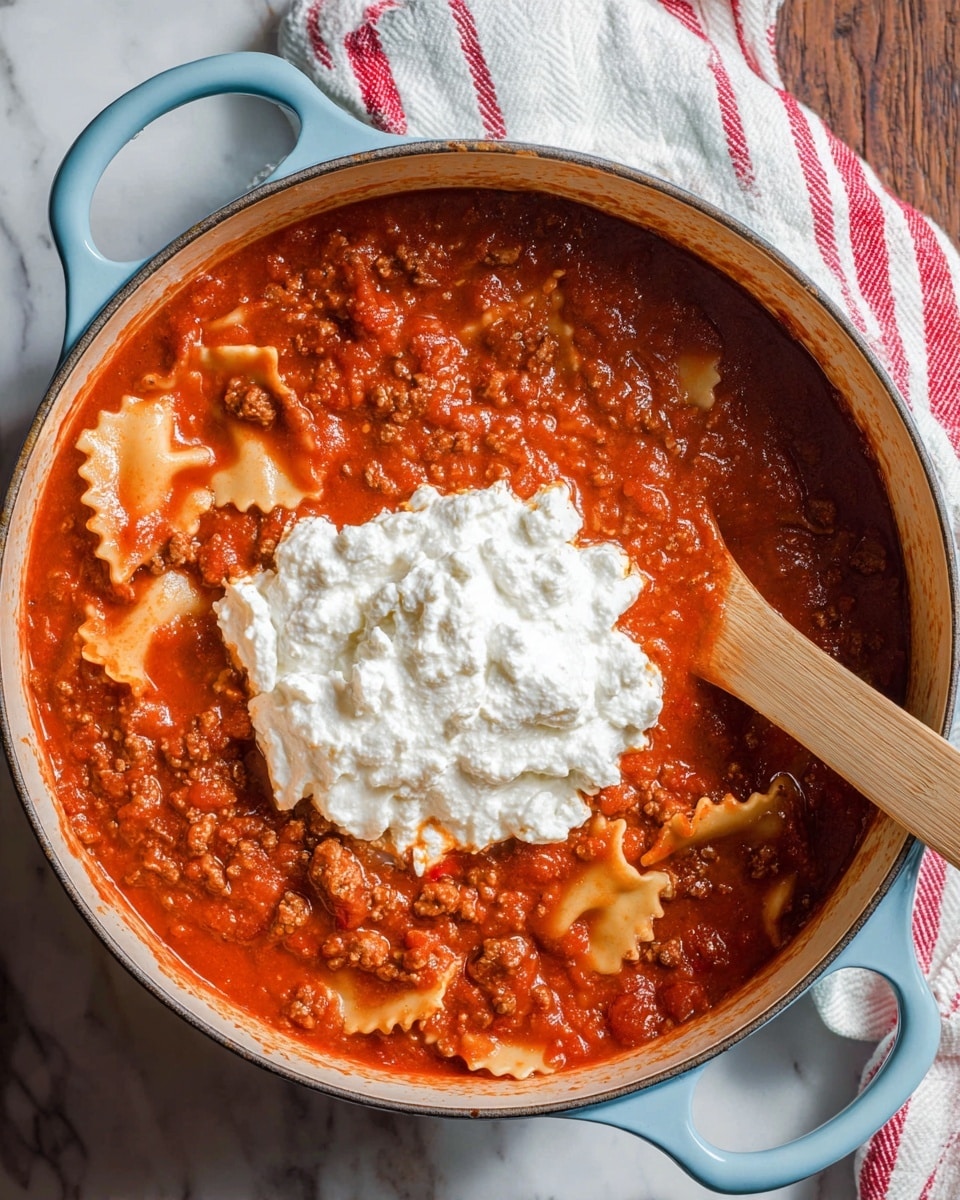 A light blue pot filled with a thick red tomato sauce with visible chunks of ground meat and scattered pieces of lasagna noodles with a wavy edge filling the sauce, topped by a large dollop of white cottage cheese in the center. A wooden spoon partially covered in the sauce rests inside the pot. The pot is placed on a white marbled surface with a white cloth that has red stripes nearby. photo taken with an iphone --ar 4:5 --v 7