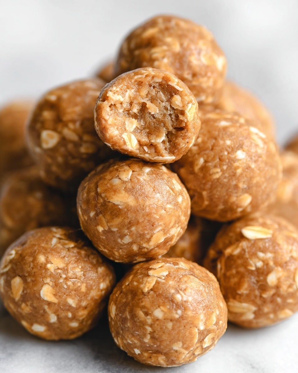 A close-up of a pile of round energy balls stacked together on a white marbled surface. Each ball is light brown with visible oat flakes mixed throughout, adding texture. The top energy ball in the center has a bite taken out, showing a soft and slightly crumbly inside filled with oats. The balls have a smooth, slightly shiny surface with irregular oat pieces on their outer layer. photo taken with an iphone --ar 4:5 --v 7
